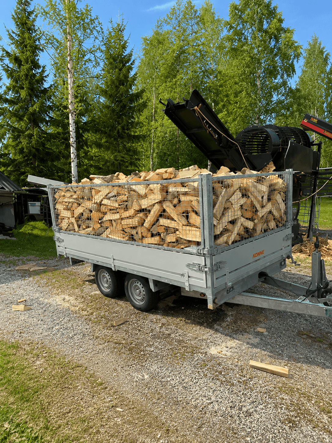 Peräkärry täynnä tuoretta koneellisesti puhdistettua koivuklapia klapikoneen vieressä